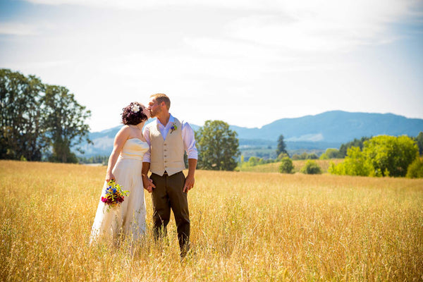 a bride and groom kiss in a field in a casual wedding setting