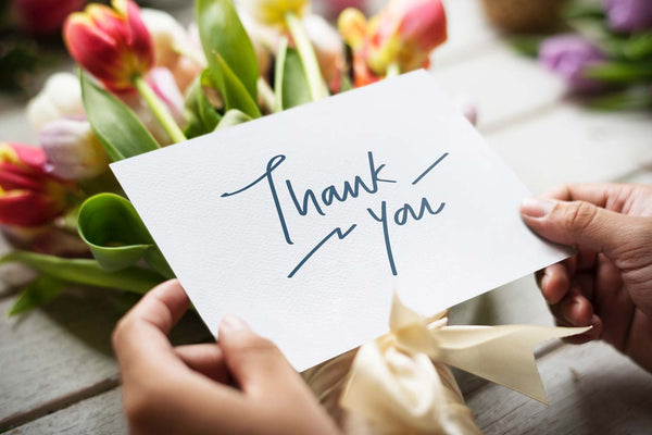 A person holds a thank you card after receiving a bunch of flowers