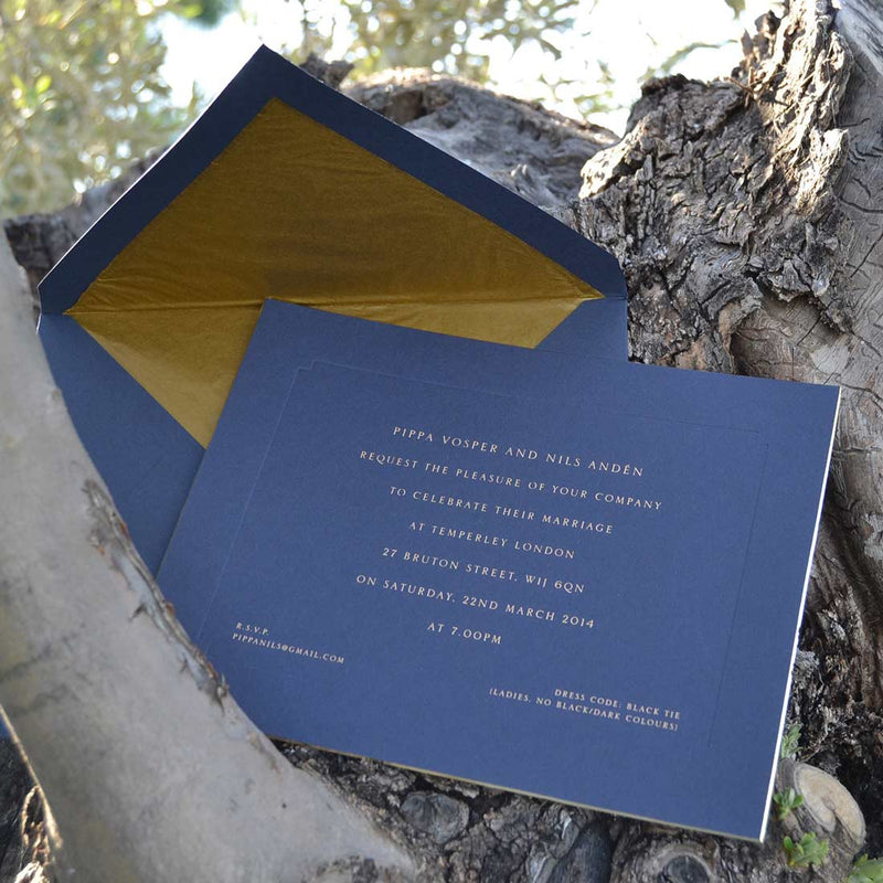 The gold engraved Birley wedding invitations are shown resting on a tree with its matching blue and gold lined tissue 
