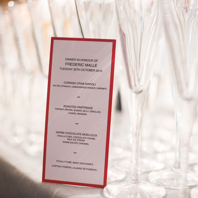 The Burlington wedding menu cards with black text on a white card and bright red border leaning on champagne glasses