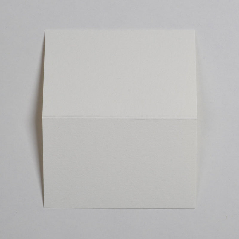 The cream Wedding name place cards shown flat on a table surface with the crease in the middle