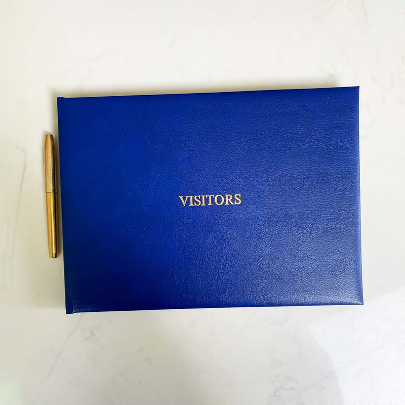 A navy blue leather bound visitors book with gold embossing on the front cover