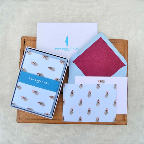 A pheasant feather pattern presented on a pale blue background, with matching rose pink envelopes and claret tissue paper lining