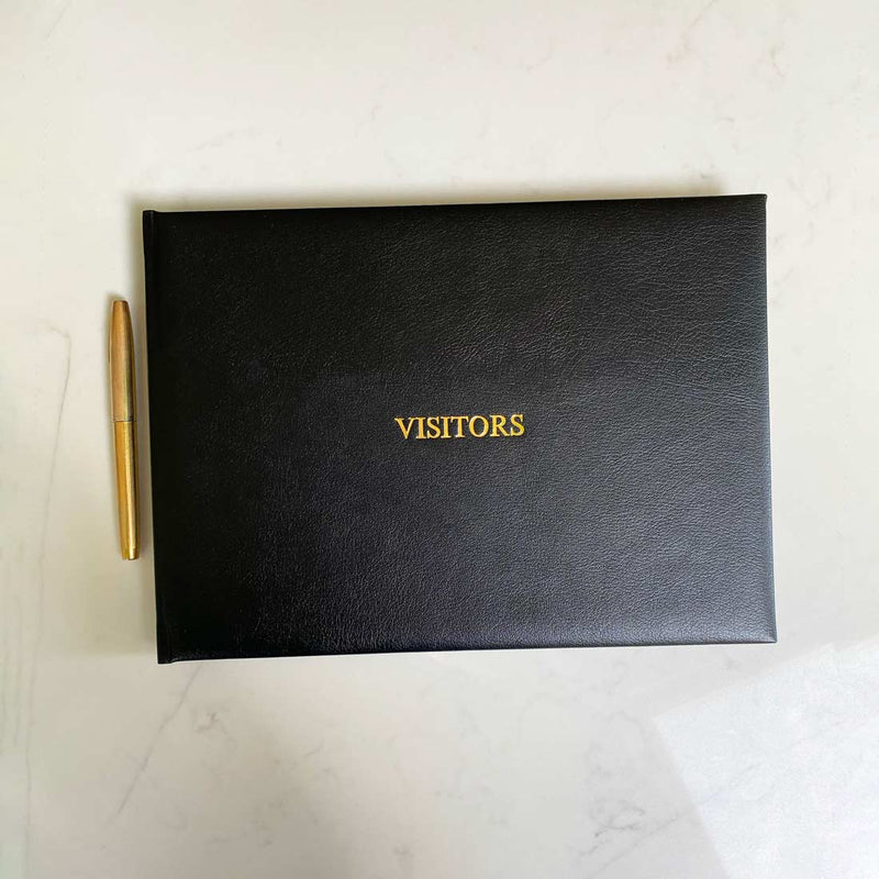 A black leather bound visitors book with gold embossing on the front cover