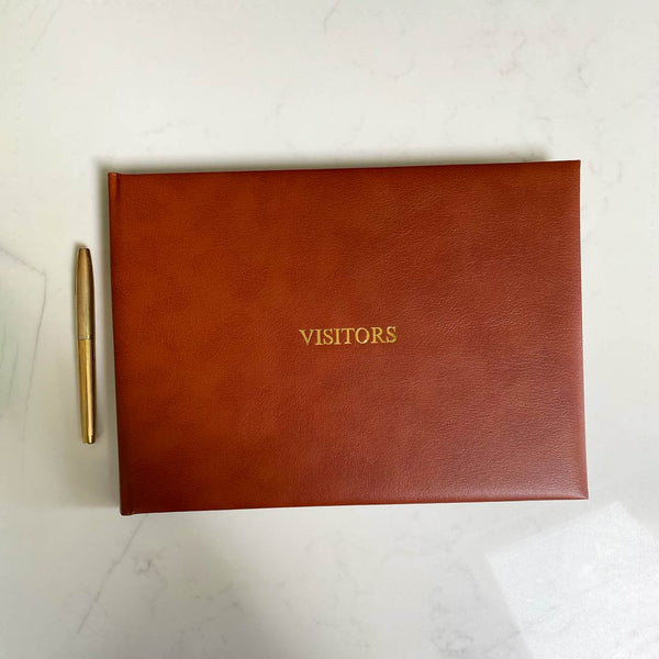 A brown leather bound visitors book with gold embossing on the front cover