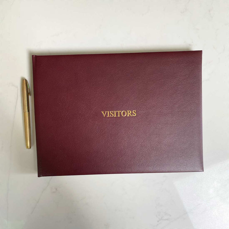 A burgundy leather bound visitors book with gold embossing on the front cover