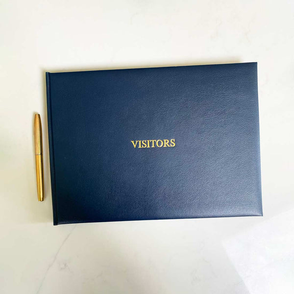 A dark blue leather bound visitors book with gold embossing on the front cover