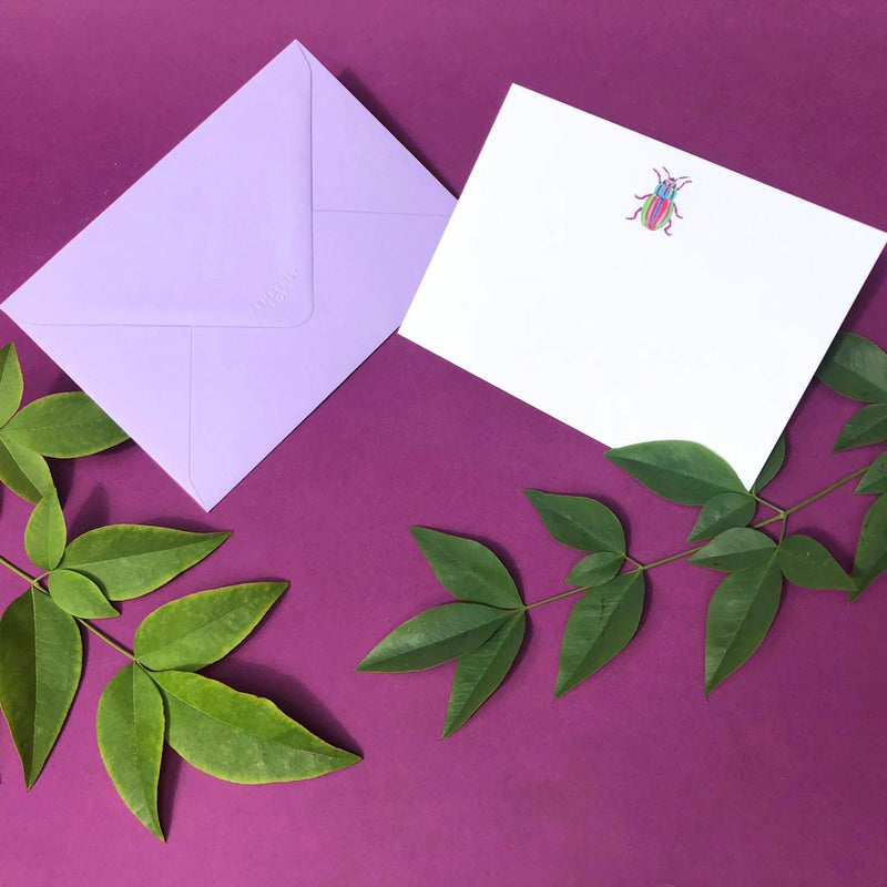 The rainbow bug note card shows a single motif sketch at the head and comes with a lavender envelope 