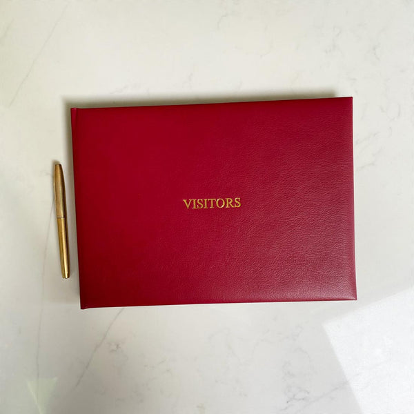 A red leather bound visitors book with gold embossing on the front cover